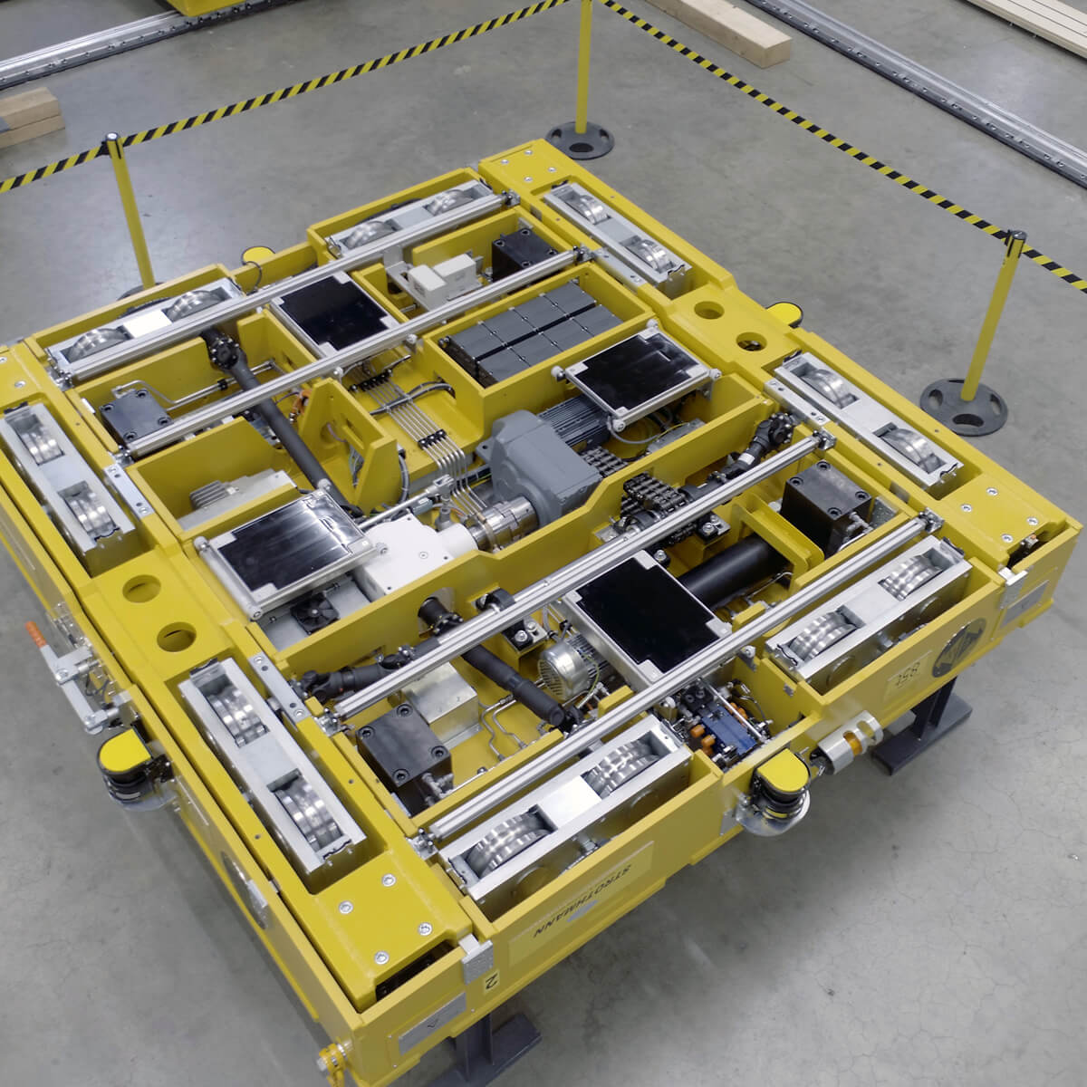 Primo piano di una piattaforma robotica gialla con vari componenti meccanici e motori, posta su un pavimento in cemento.